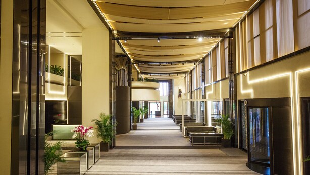 A hotel corridor with a carpeted floor, seating areas, and potted plants. - Regency Art Hotel Macau (Taipa)