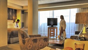 Habitación de hotel con sofá, mesa de comedor con desayuno, televisión y ventana con cortinas.
