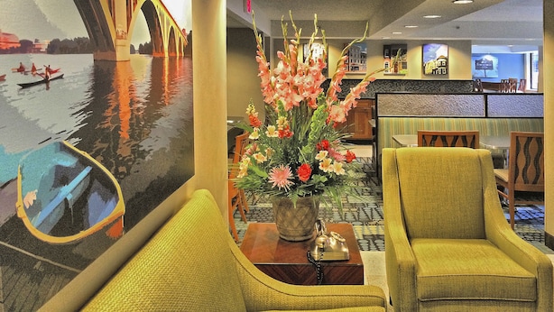 Vestíbulo de hotel con un mural grande de un puente, un centro de mesa floral y sillones tapizados en amarillo.