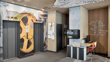 An office space with a large, circular, yellow structure, a wall-mounted ATM, and recycling bins.