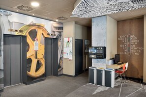An office space with a large, circular, yellow structure, a wall-mounted ATM, and recycling bins. - ibis Budapest City (Budapest)