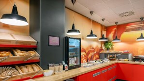 Zona de desayuno tipo buffet con diversas opciones de alimentos, un refrigerador y un reloj en la pared.