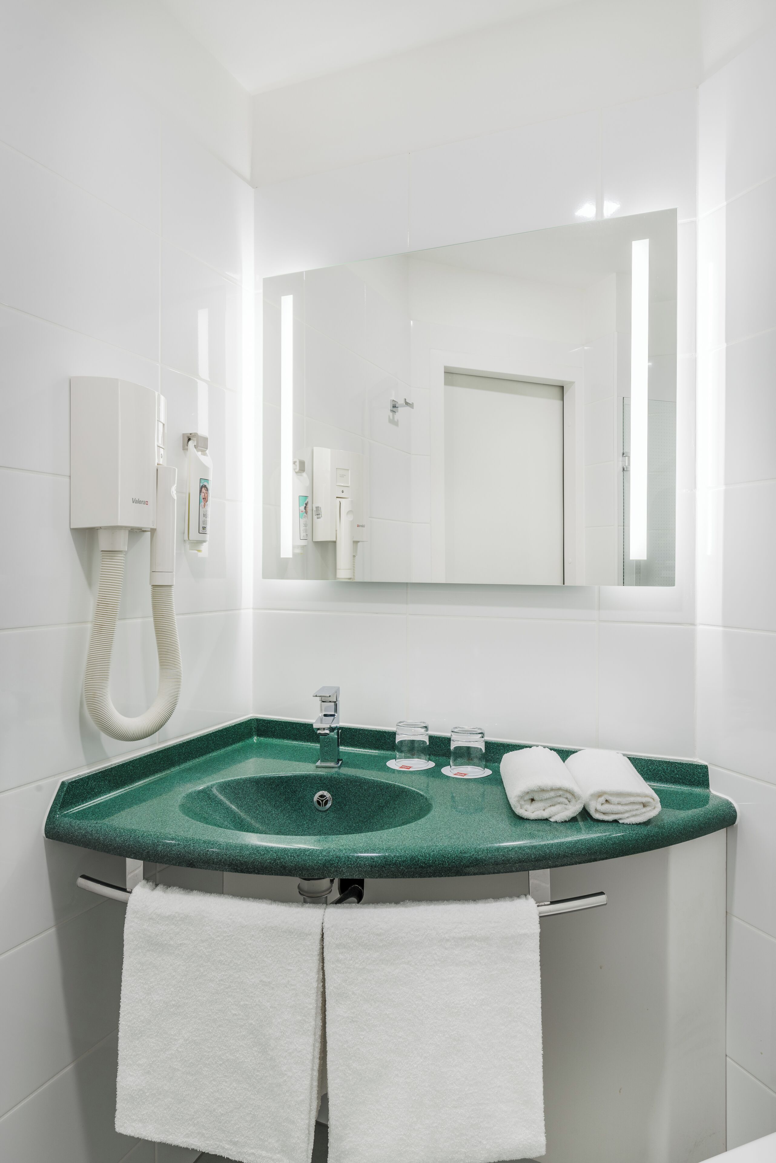 Un baño con un lavamanos verde, toallas blancas, un espejo y un inodoro blanco.