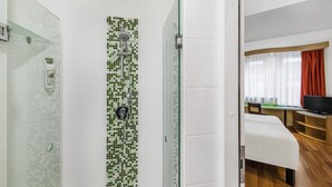 Habitación de hotel con ducha, cama, escritorio y televisor.