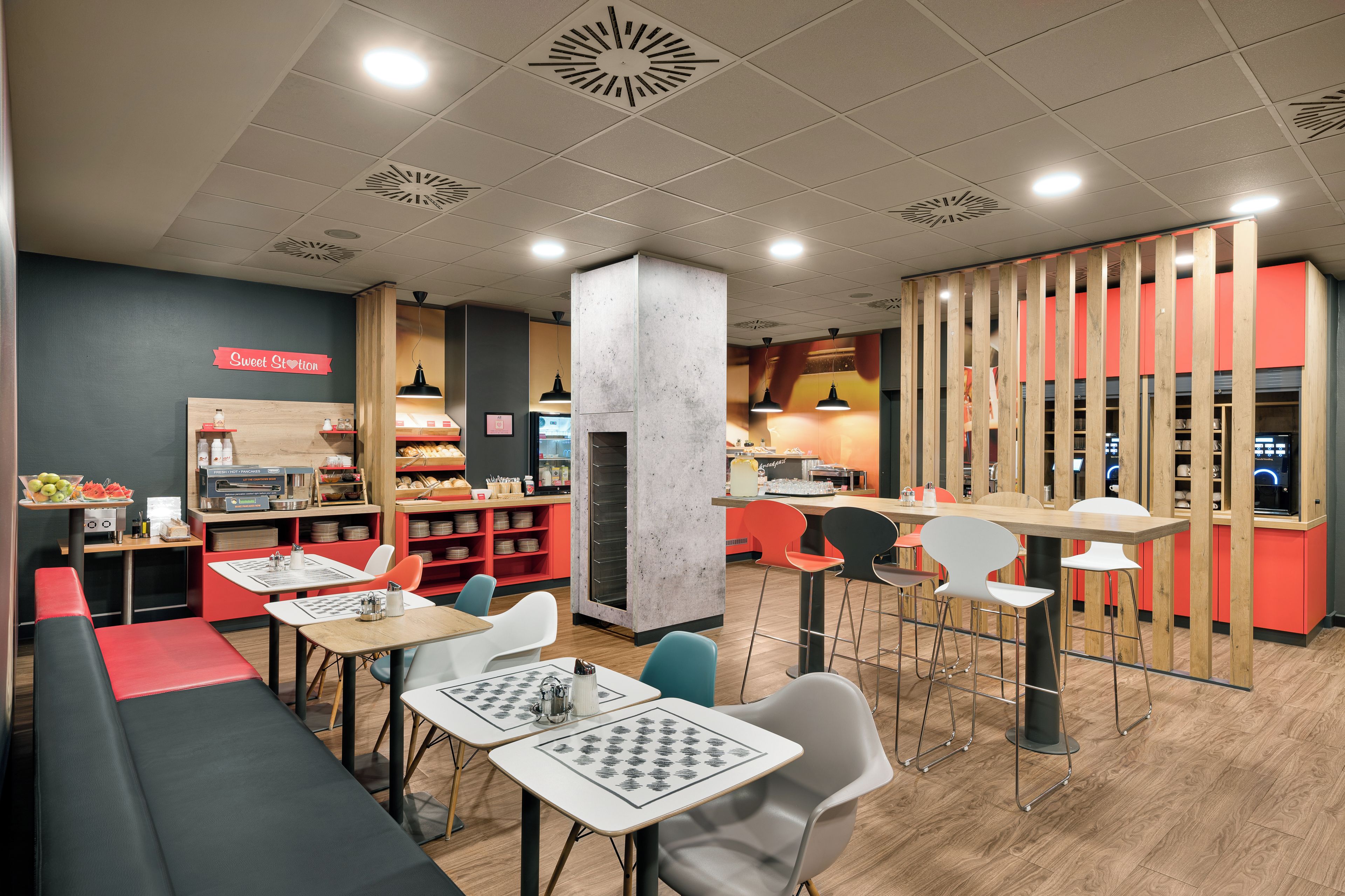 Un café moderno con varios espacios de estar, mesas y sillas, y una barra visible con productos alimenticios.