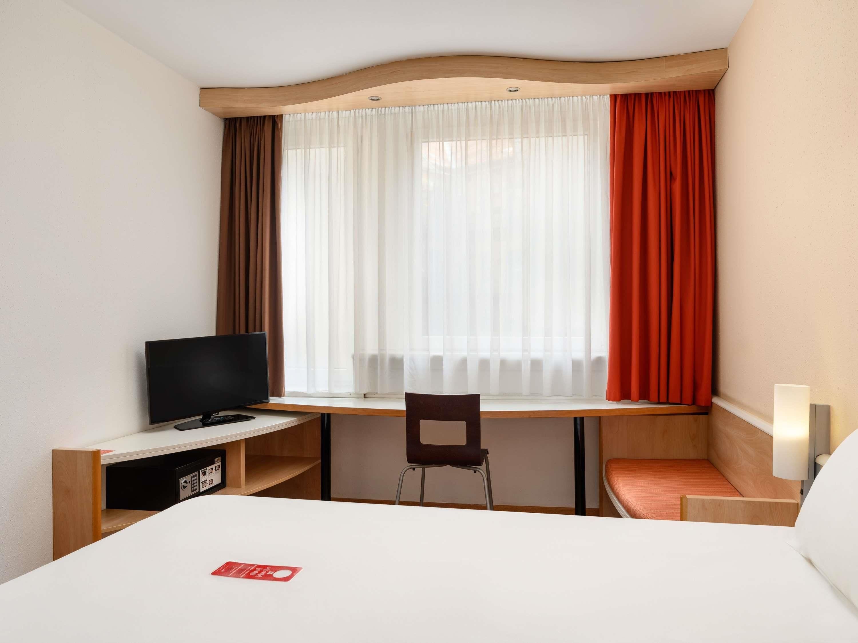 A hotel room with a bed, a desk, a chair, a television, and a window with curtains.