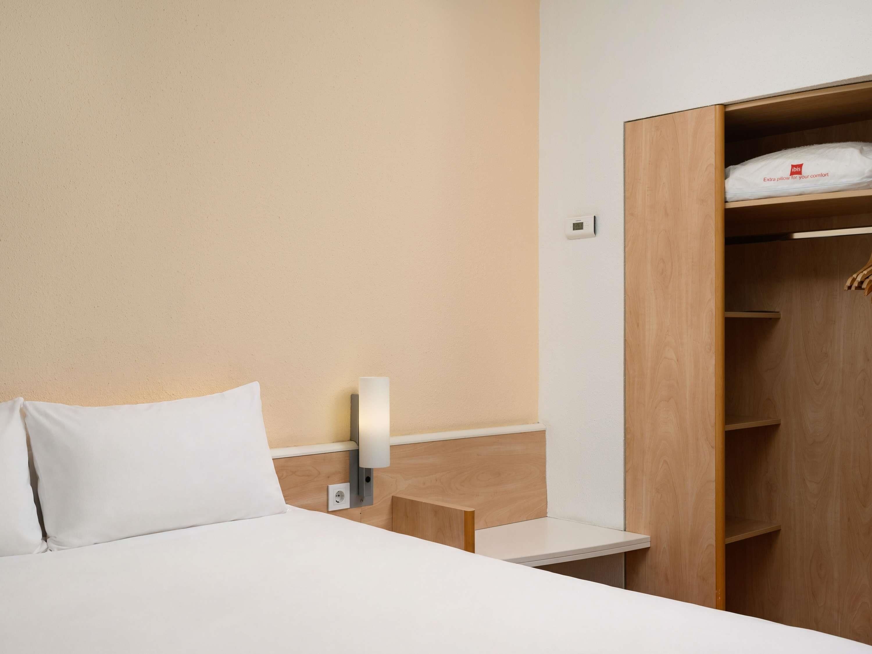 A hotel room with a bed, a bedside table, a wardrobe, and a wall-mounted light.