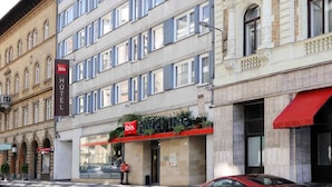 A hotel with a modern facade, multiple windows, and a red awning. - ibis Budapest City (Budapest)
