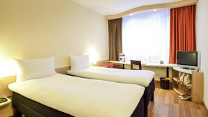 A hotel room with two beds, a desk with a computer, a chair, a TV, and a window with curtains. - ibis Budapest City (Budapest)