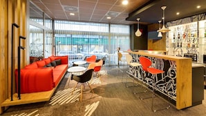 A modern interior with a red sofa, a bar area, and a view of the street. - ibis Budapest City (Budapest)