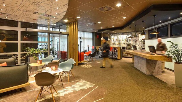 A modern interior with a reception desk, seating area, and a bar. - ibis Budapest City (Budapest)