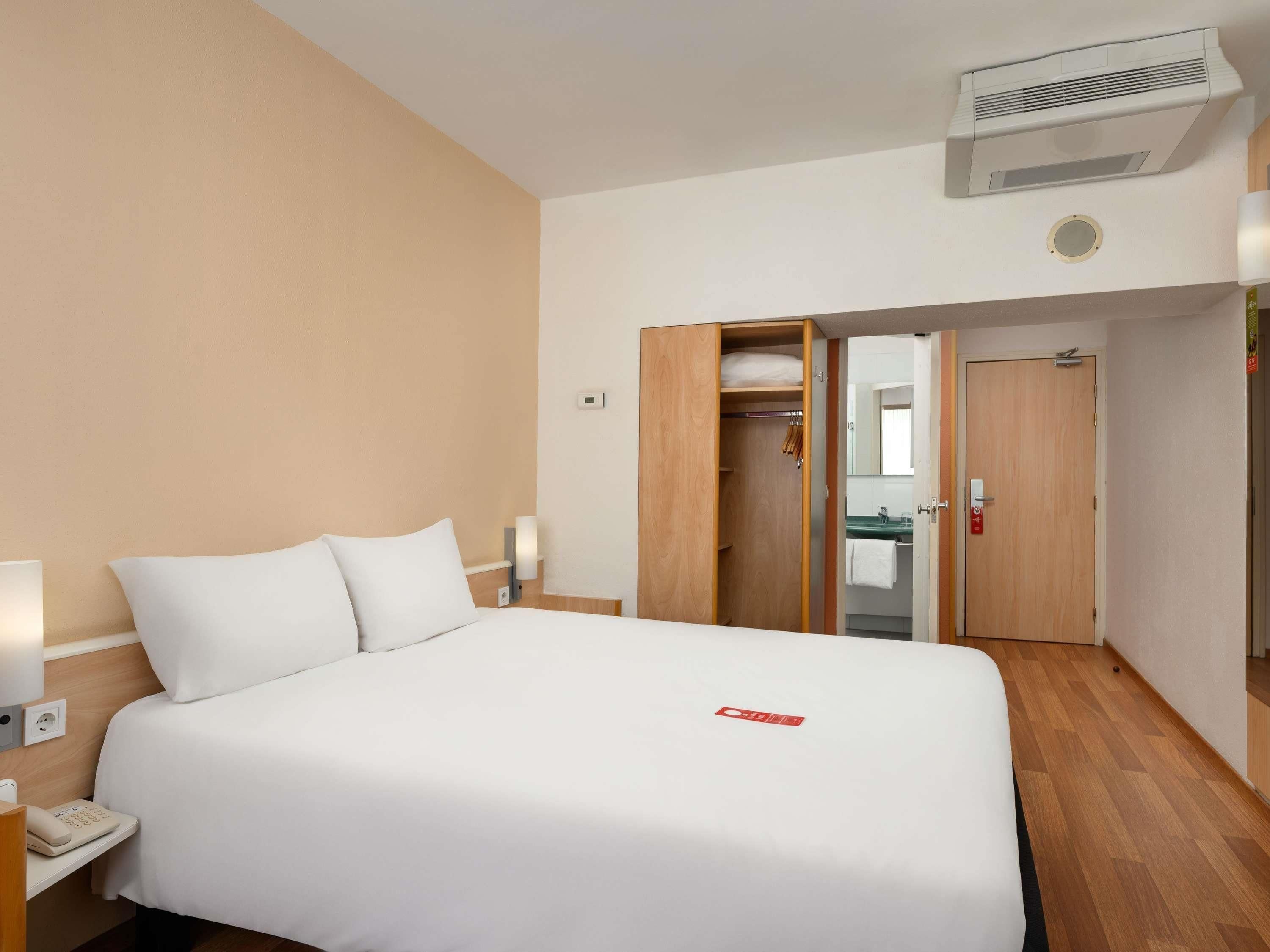 A hotel room with a bed, bedside table, lamp, and a wardrobe with a mirror.