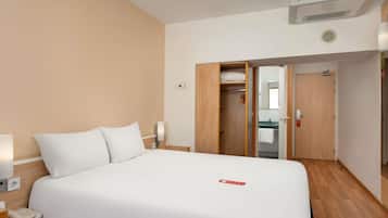 A hotel room with a bed, bedside table, lamp, and a wardrobe with a mirror.