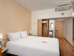 Una habitación de hotel con cama, mesita de noche, lámpara y armario con espejo.