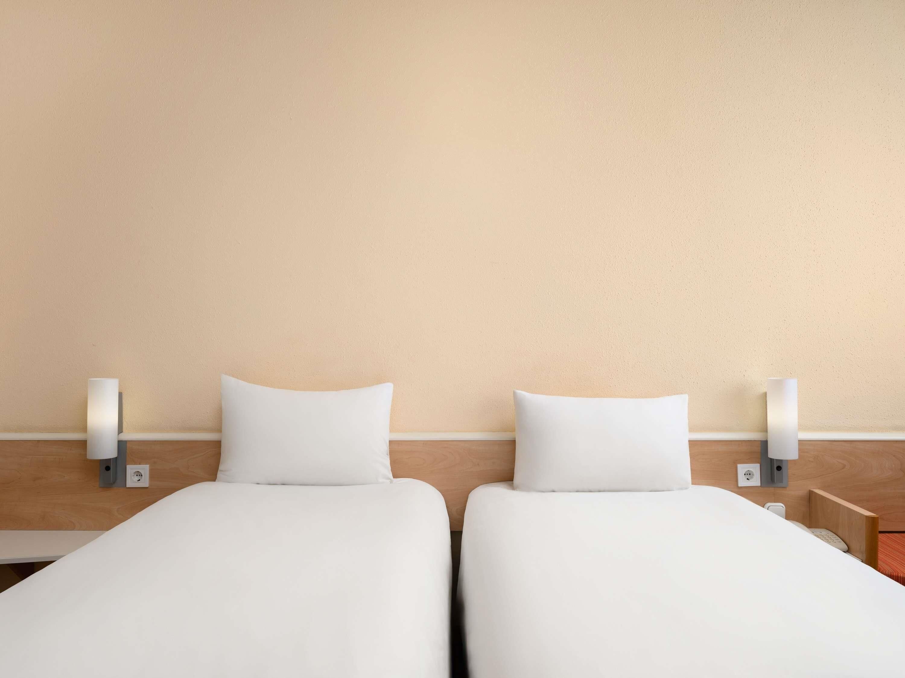 A hotel room with two beds, each with a pillow and a nightstand with a lamp.