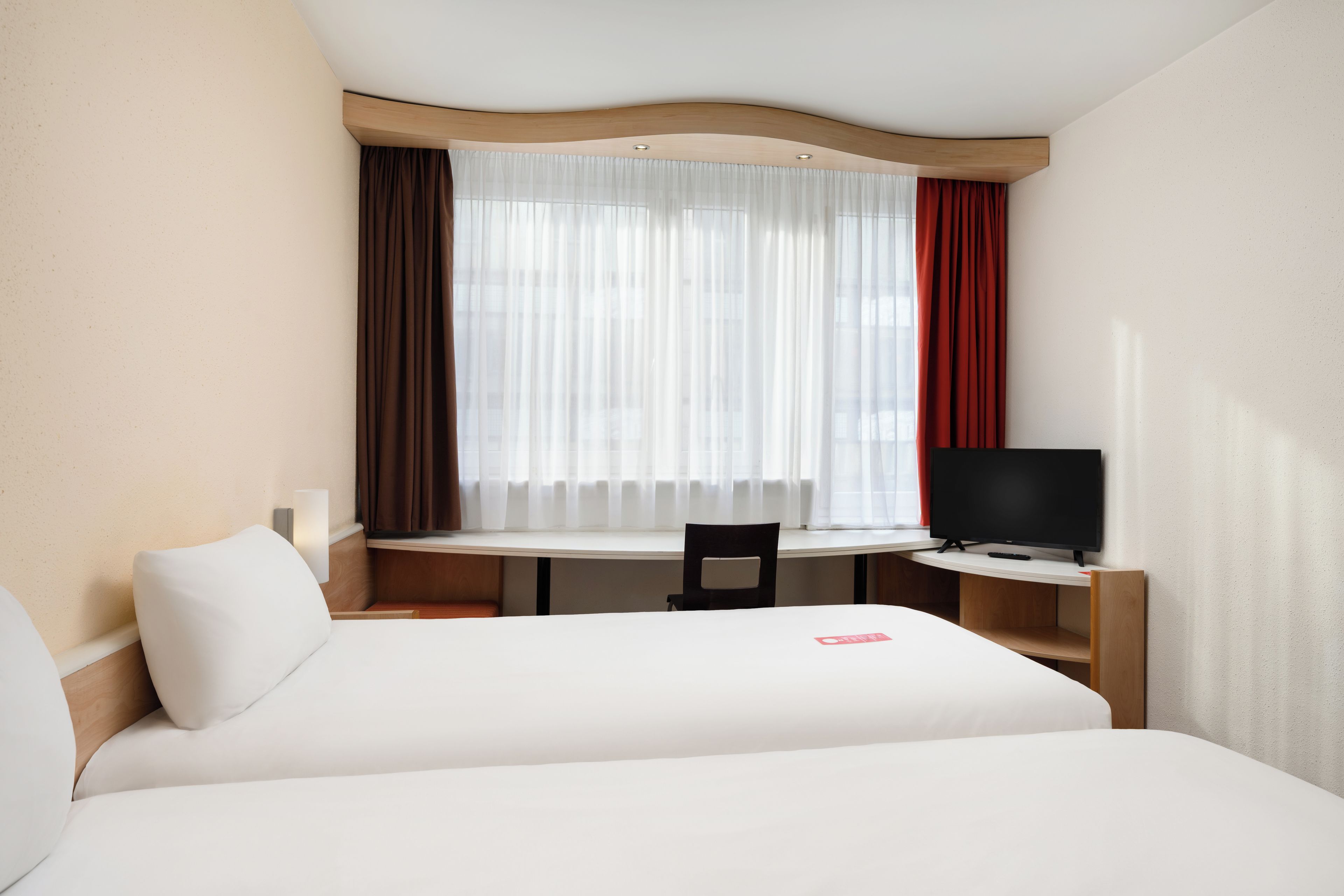 A hotel room with a bed, a desk, a chair, and a television.