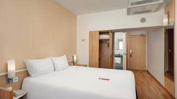 Habitación de hotel con cama, lámparas de noche, teléfono, aire acondicionado y armario.