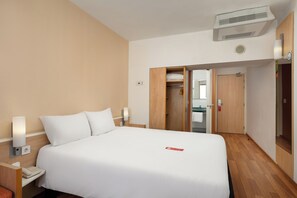 A hotel room with a bed, bedside lamps, a phone, an air conditioning unit, and a wardrobe. - ibis Budapest City (Budapest)