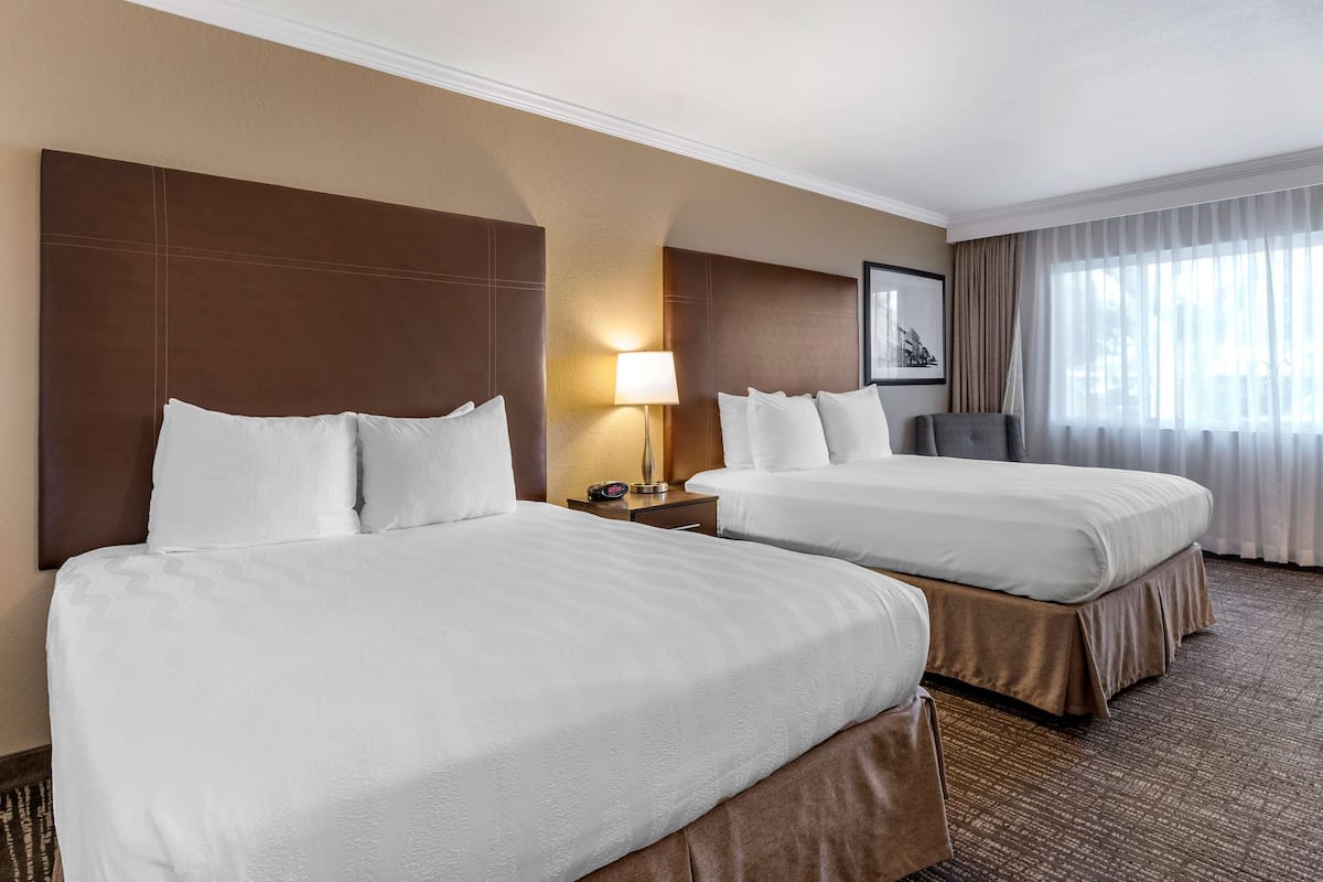 A hotel room with two beds, a nightstand with a lamp, a framed picture on the wall, and a window with curtains.