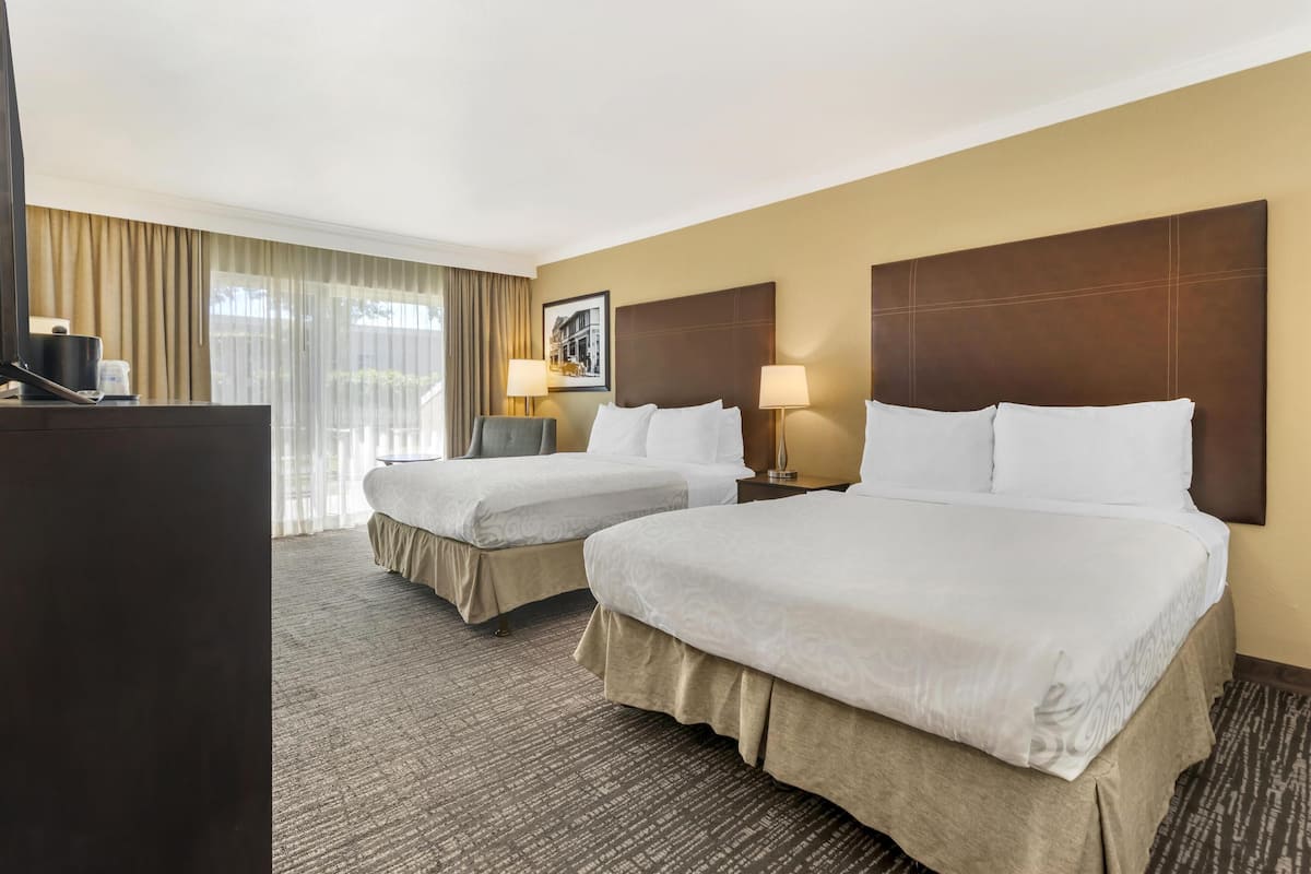 A hotel room with two beds, a desk, a chair, and a large window with curtains.