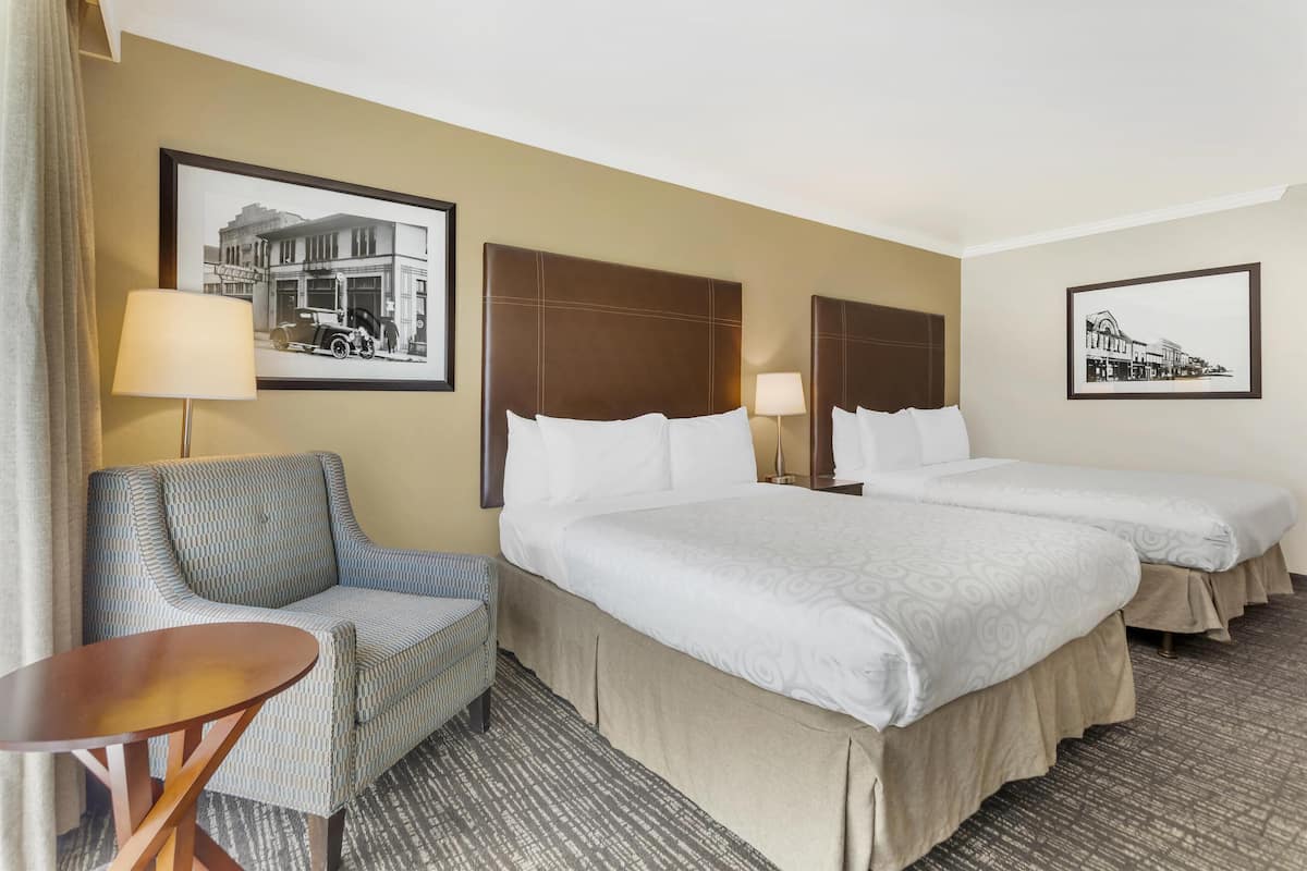 A hotel room with two beds, a sofa, a small table, and two wall-mounted lamps.