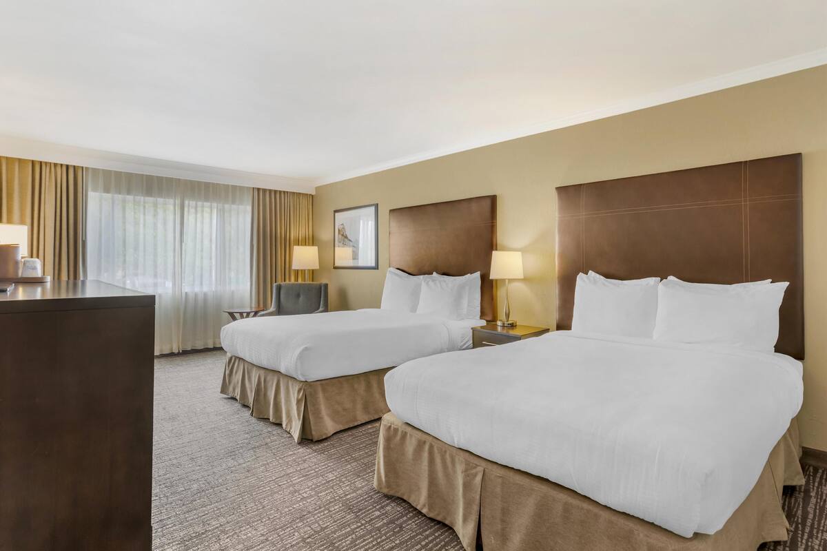 A hotel room with two beds, a desk, and a chair.