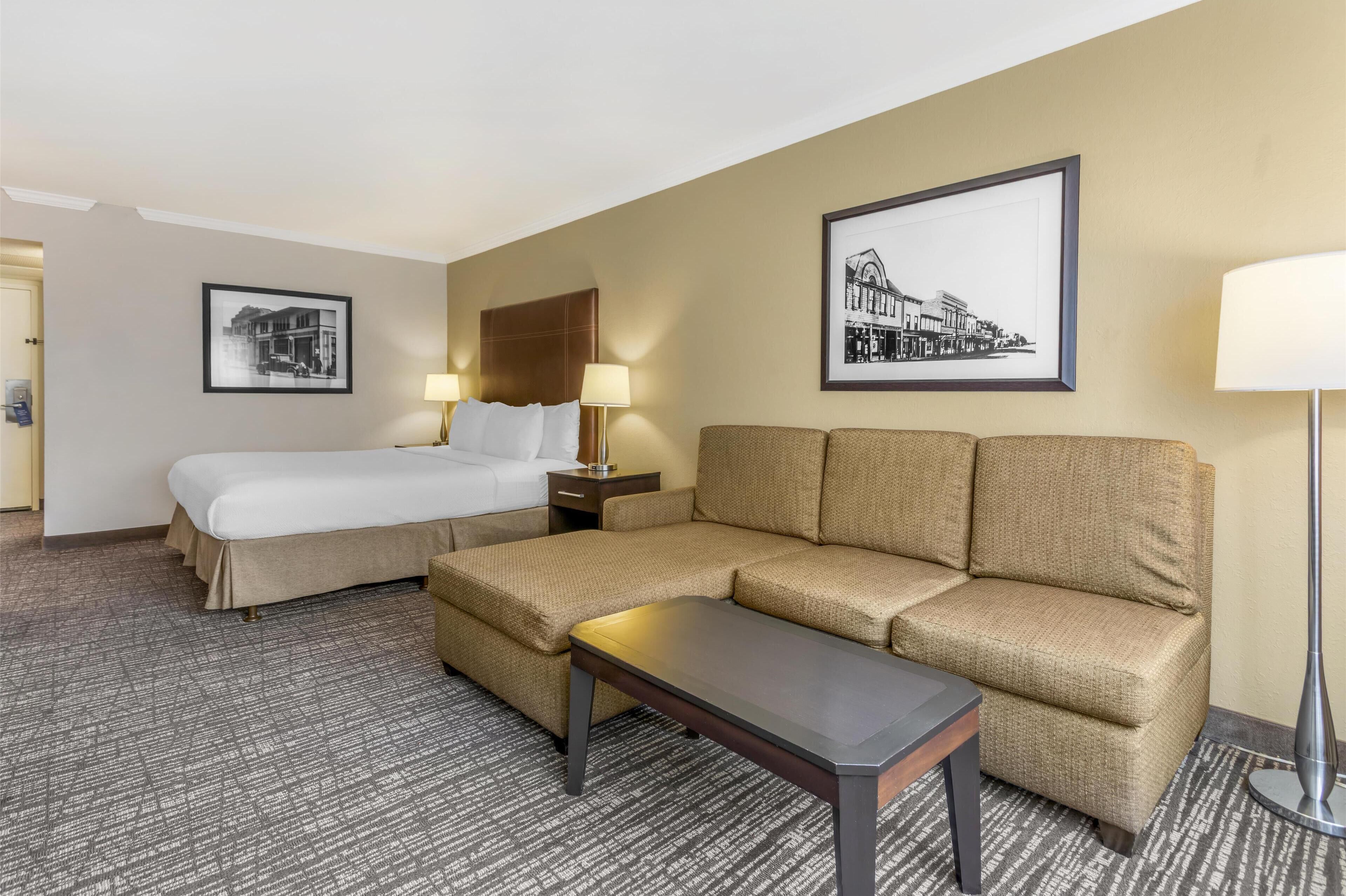 A hotel room with a bed, a sofa, a small table, two lamps, and two framed pictures on the walls.
