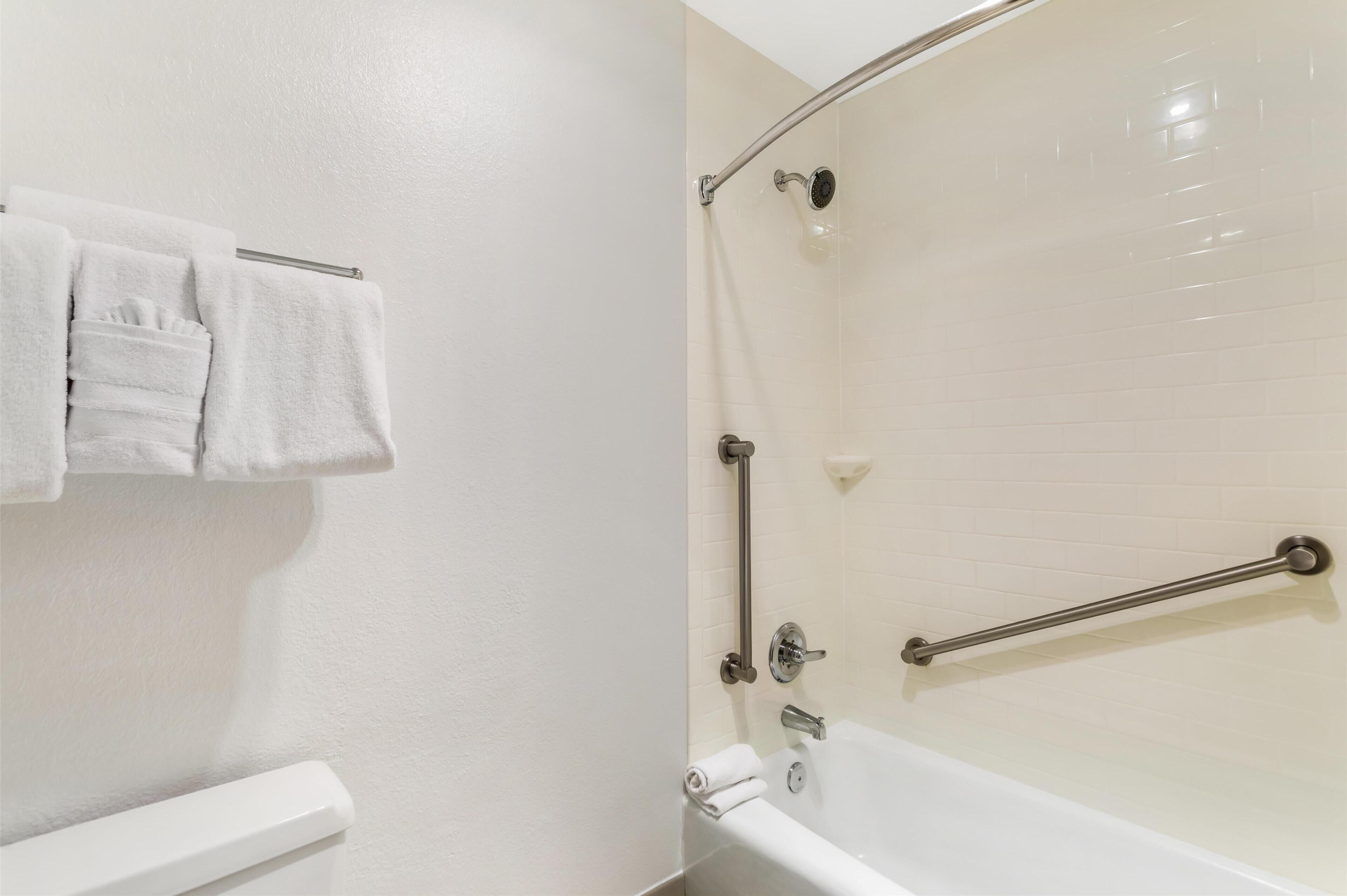 A bathroom with a bathtub, a towel rack with towels, and a grab bar for safety.