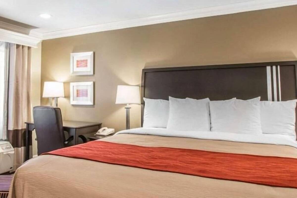 A hotel room with a bed, two bedside lamps, a desk with a telephone, and a chair.