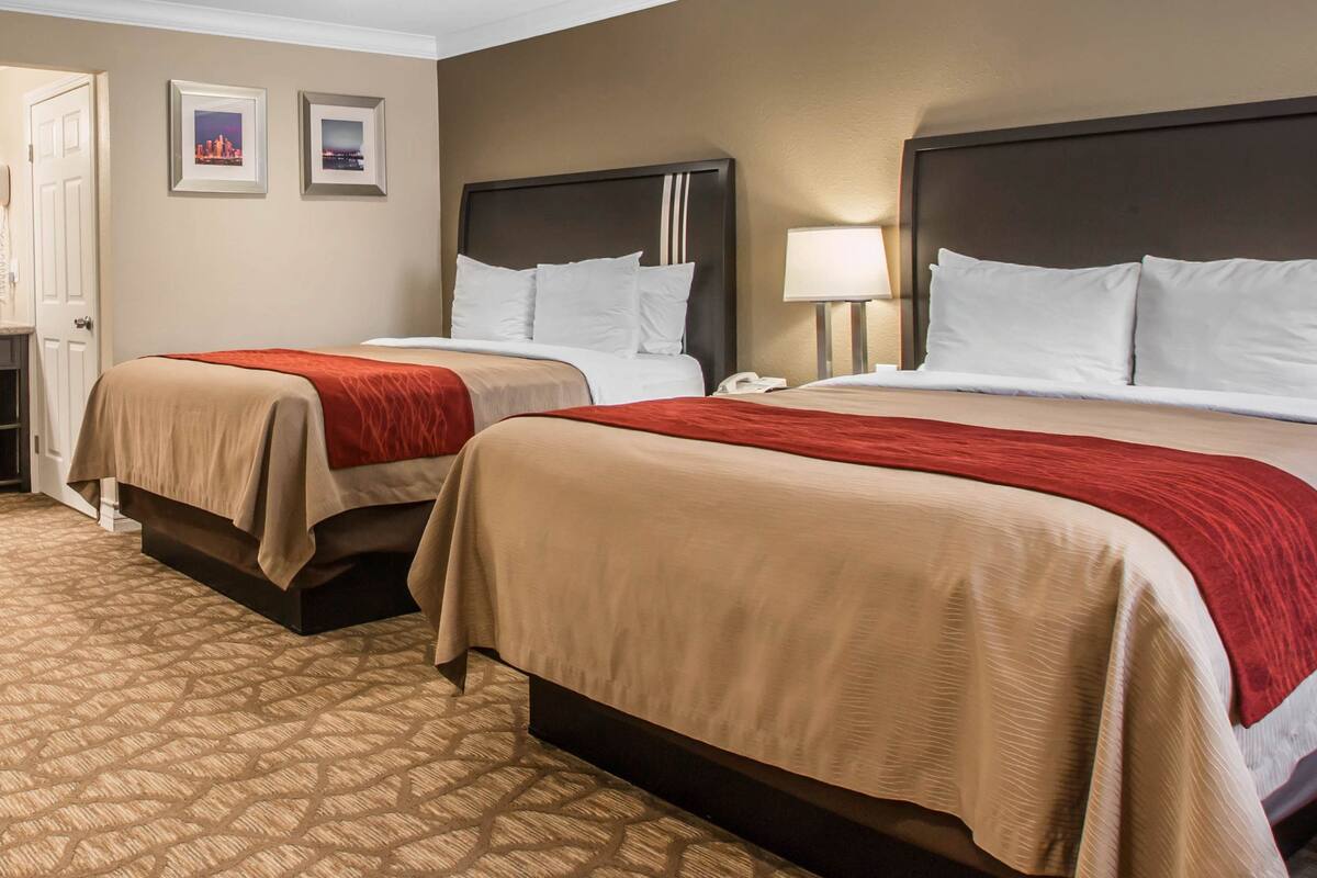 A hotel room with two beds, beige and red bedding, a patterned carpet, and a cityscape view.