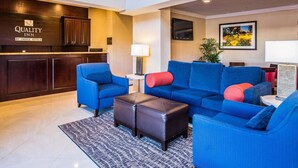 A hotel lobby with a reception desk, blue sofas, a coffee table, and a painting on the wall.