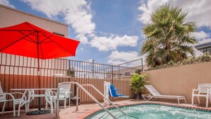 A pool area with lounge chairs, a red umbrella, and a palm tree.