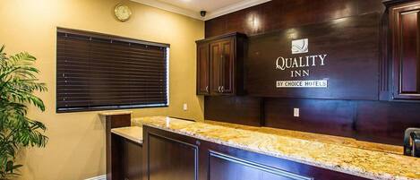 A kitchen with dark wood cabinets, a granite countertop, and a sign for 'Quality Inn by Choice Hotels'.
