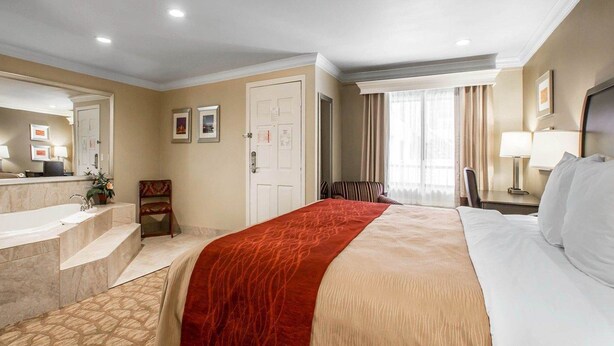 A hotel room with a bed, a desk, a chair, a bathroom with a sink, and a mirror.