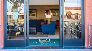 A hotel entrance with a sliding door, a green doormat with the hotel name, a blue sofa inside, and a wheelchair-accessible sign outside.