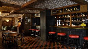 A bar area with checkered flooring, wooden bar stools, and a well-stocked liquor shelf.