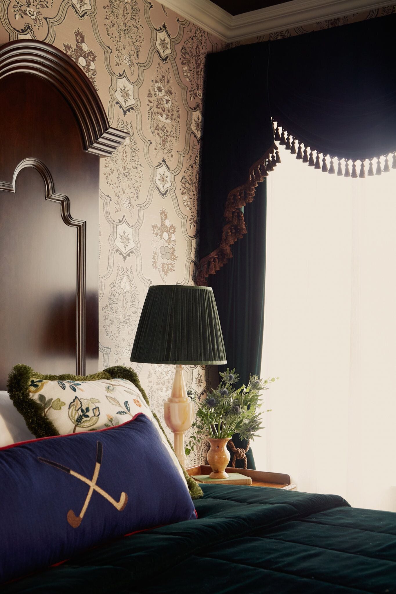 Een slaapkamer met een bed, nachtkastje, lamp en raam met gordijnen.