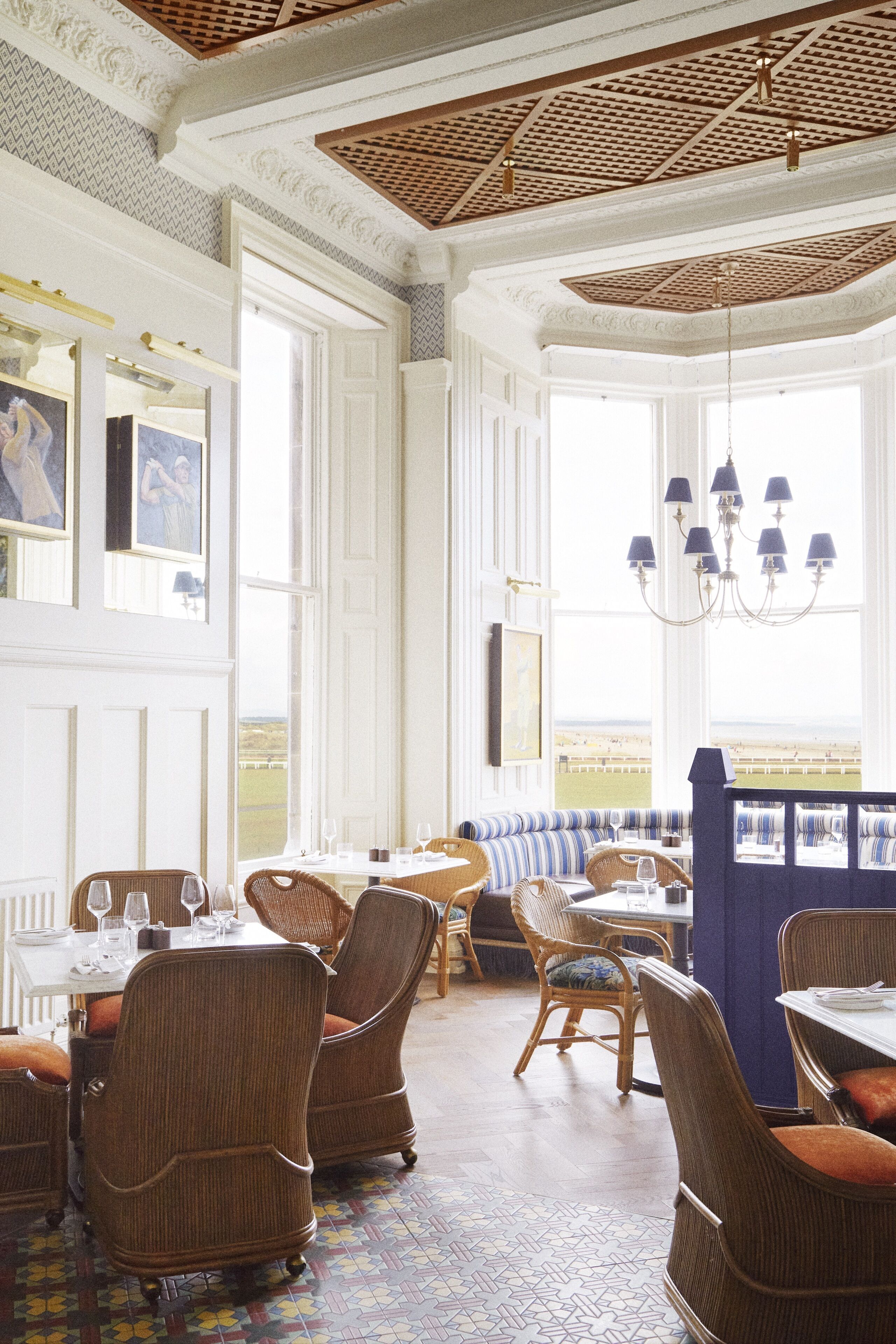A dining area with wicker chairs, a patterned floor, and a view through a large window.