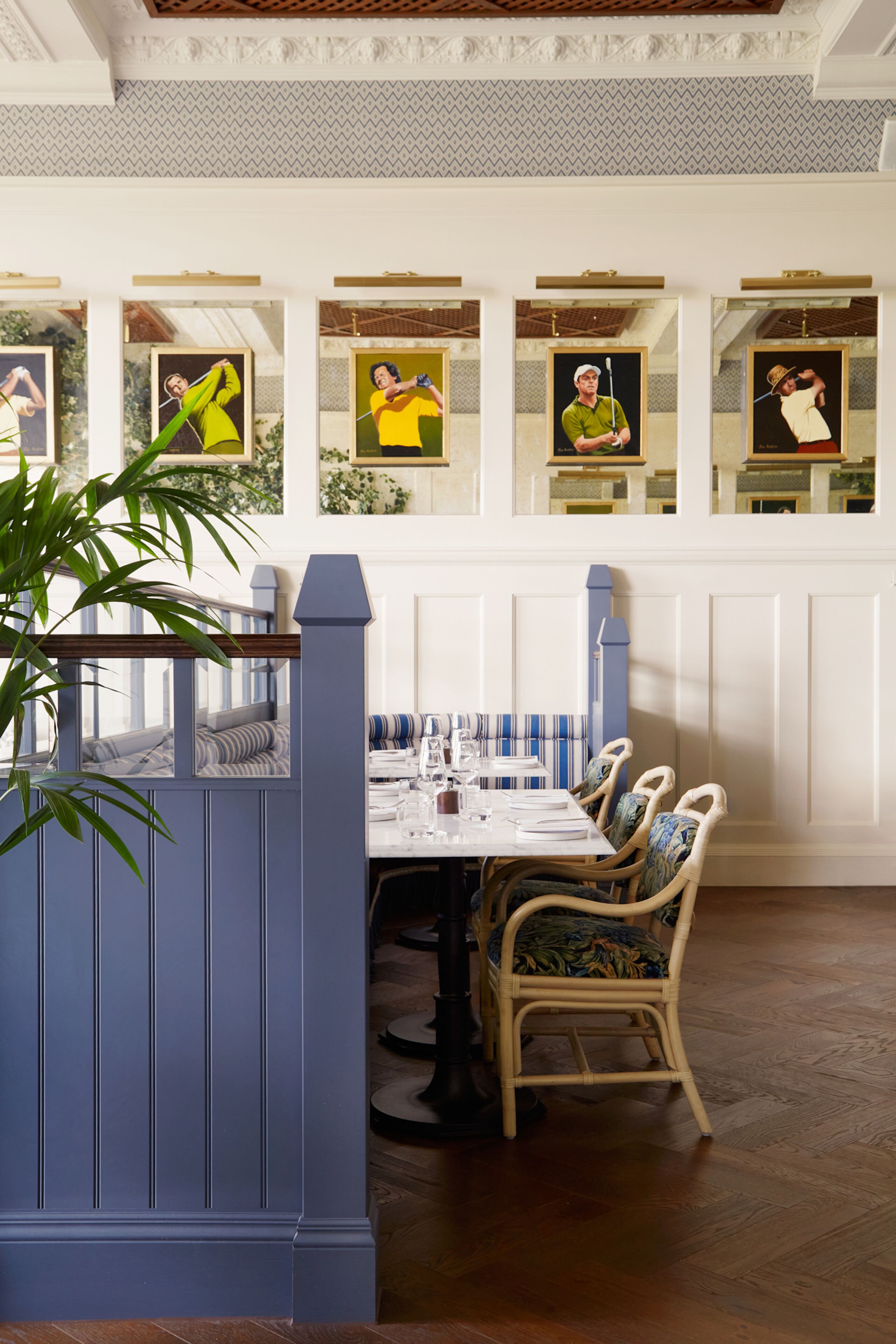 A dining area with a table set for four, surrounded by wicker chairs. There are framed artworks on the wall above the table.
