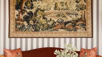 A room with a large tapestry, a brown sofa, a vase with plants, and striped wallpaper.