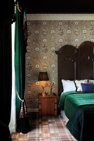 A bedroom with a wooden headboard, a green bedspread, a patterned wallpaper, and a plaid floor.