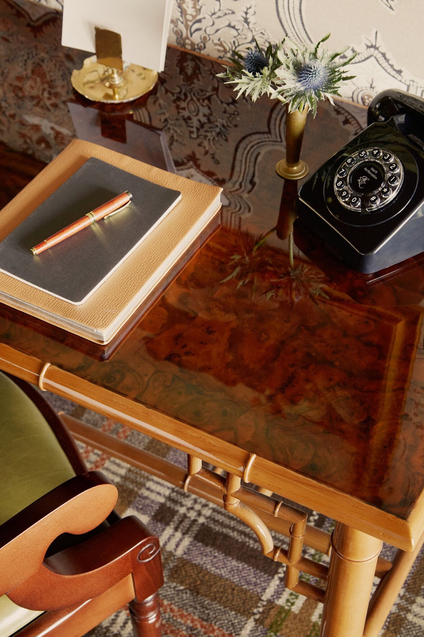 A wooden desk with a notebook, pen, and a telephone.