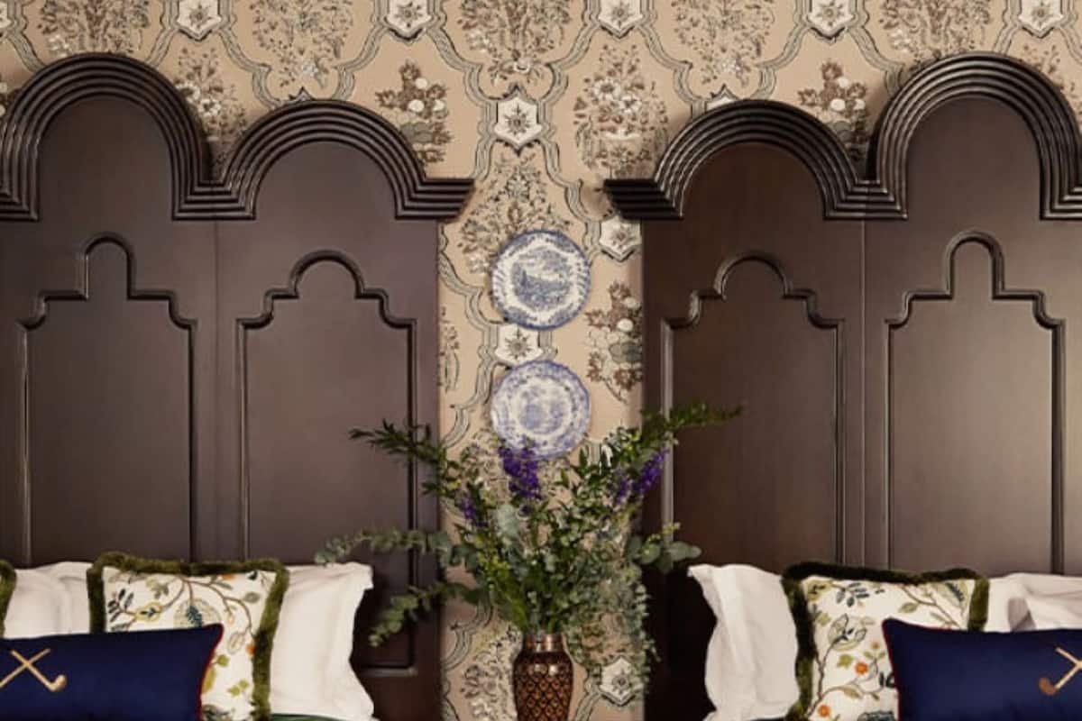 A room with two beds, a nightstand, a vase with flowers, and a patterned wallpaper.