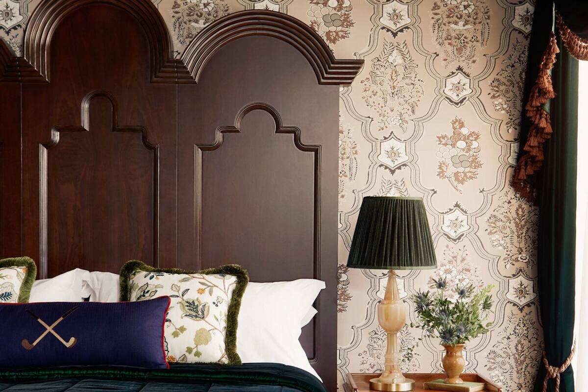 A bedroom with a large bed, a wooden nightstand, a lamp, and a decorative wall.