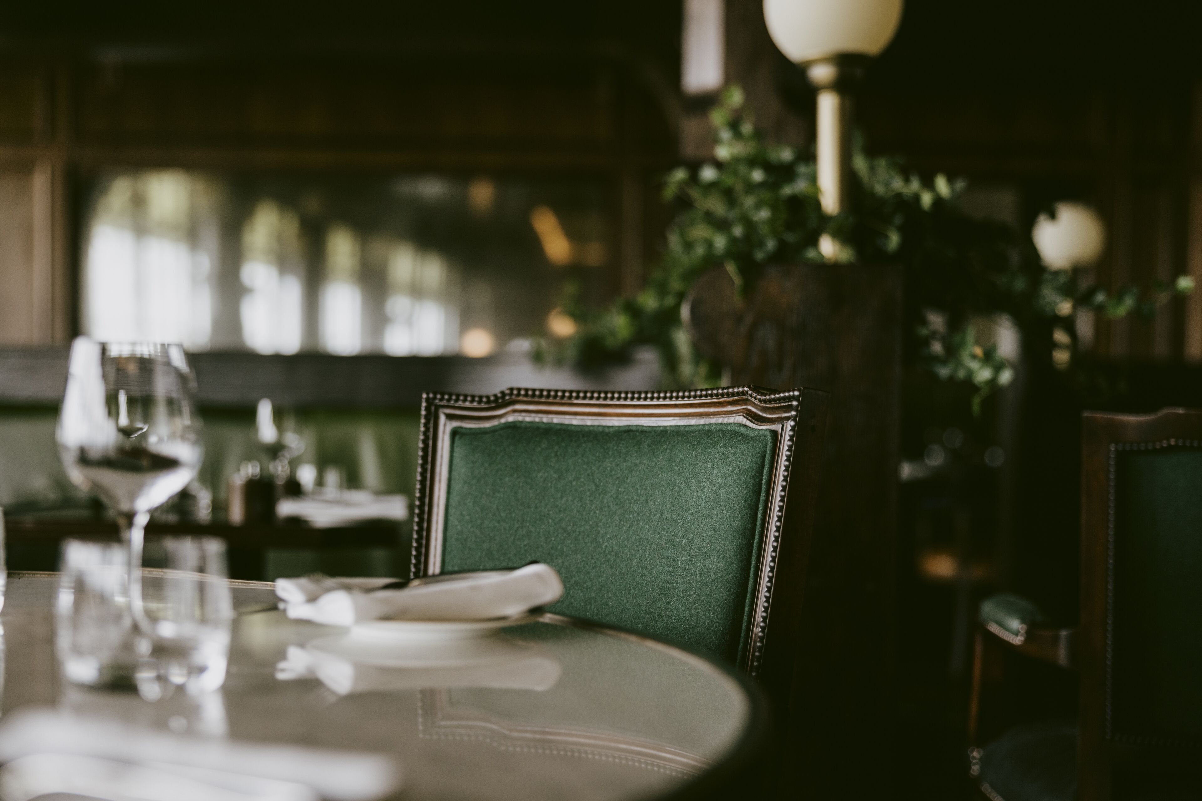 A dining table with a green upholstered chair, a wine glass, and a candle.