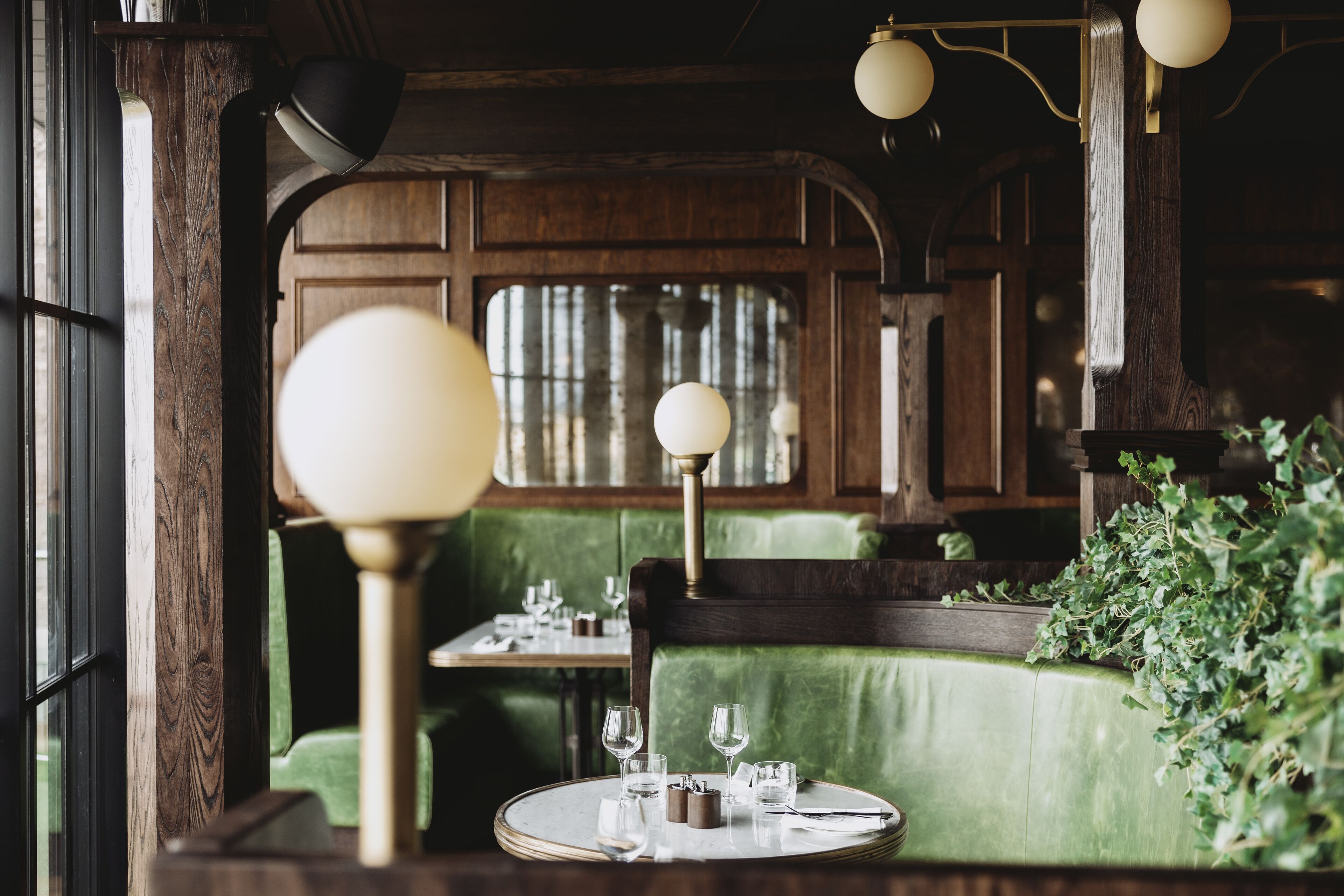 A cozy restaurant with green upholstered booths, round tables, and hanging pendant lights.