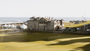 A large, historic building with multiple stories and a prominent entrance, situated next to a golf course with a clear view of the ocean.