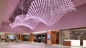 A spacious lobby with a modern reception desk, seating area, and a unique ceiling light installation. - Hilton Washington DC National Mall The Wharf (Washington)