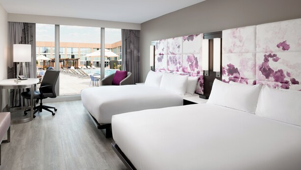 A hotel room with two beds, a desk, a chair, and a view of the pool area. - Hilton Washington DC National Mall The Wharf (Washington)