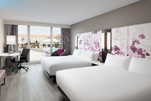 Ein Hotelzimmer mit zwei Betten, einem Schreibtisch, einem Sessel und Blick auf den Poolbereich.